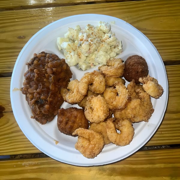 A plate of Hank's Catfish & BBQ fried shrimp, baked beans, potato salad, and hushpuppies.