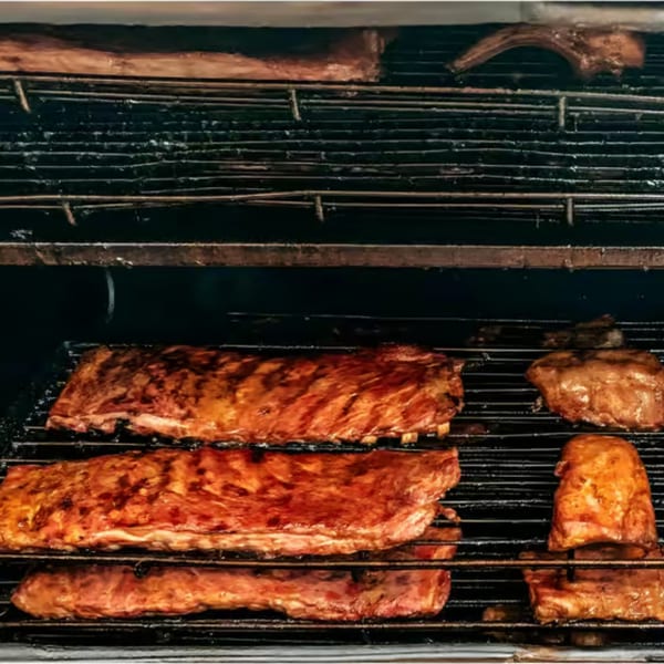 Hank's Catfish & BBQ ribs and other meats cooking on a dark, multi-level smoker rack.