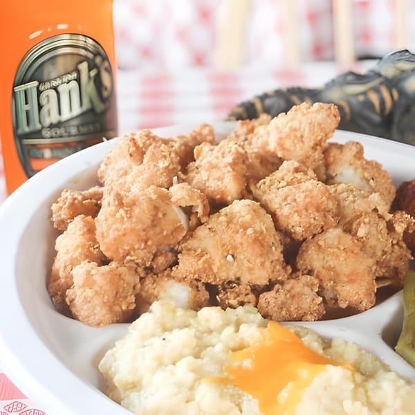 Hank's Catfish & BBQ fried catfish nuggets, grits with cheese, and pickles on a white plate.