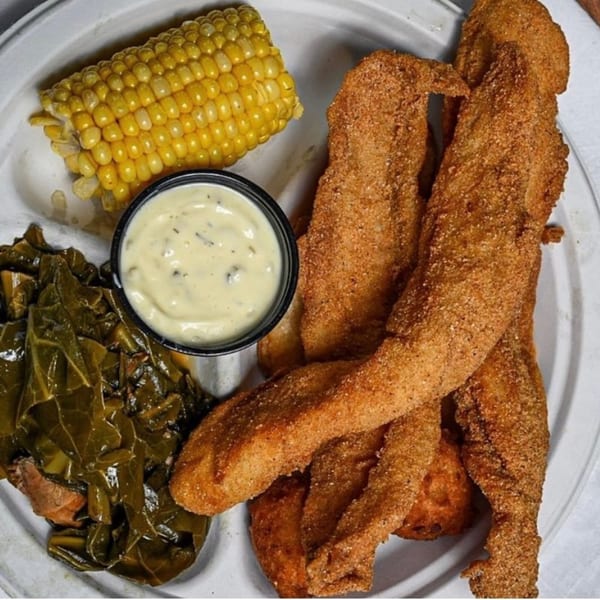 A plate of Hank's Catfish & BBQ fried catfish, collard greens, corn on the cob, and tartar sauce.